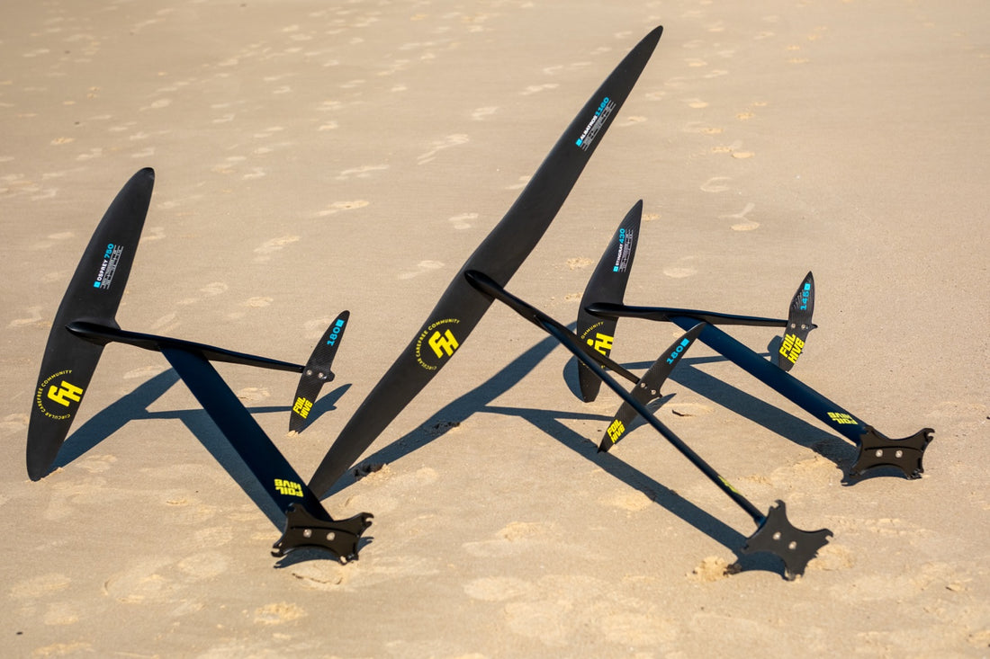 Three complete FoilHive foil setups standing on a sand beach, with front wings of different sizes
